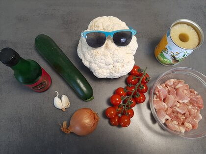Ingrediënten voor recept: bloemkoolrijst met kip, ananas, courgette, cherrytomaatjes, ui en knoflook.