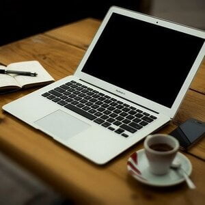 Een laptop met kopje koffie en schrijfblok.